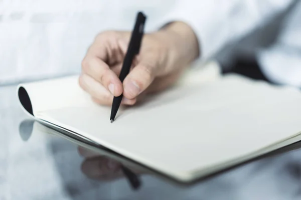 Een handschrift in een dagboek op een glazen tafel. Gericht op een hand met pen — Stockfoto