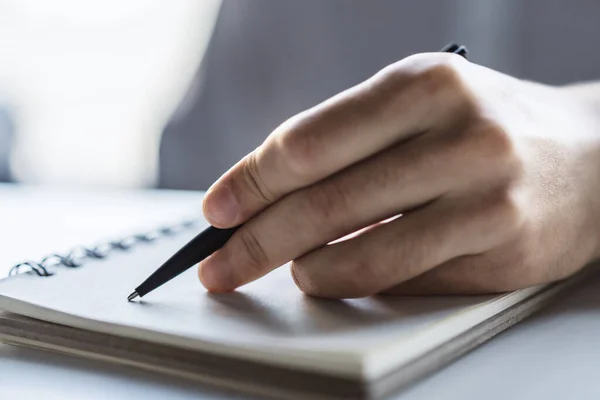 Close-up van de man hand schrijven in notitieblok op een witte tafel. Gericht op een hand met pen — Stockfoto