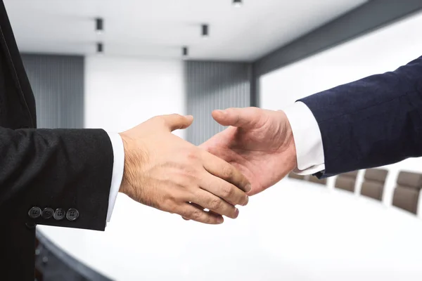 Two businessmen shake hands in a meeting room, closeup