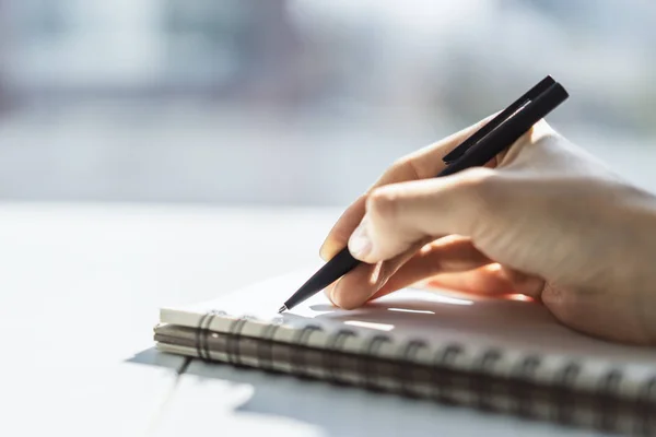 Woman writes with a pen in notebook in a sunny office, business and education concept. Close up — Stock Photo, Image