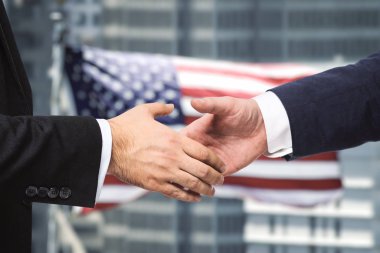 ABD bayrağının arka planında iki işadamının el sıkışması, bir sözleşme imzalanması,