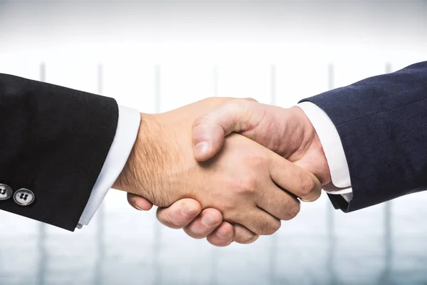 Two businessmen shake hands on the background of empty modern office, signing of a contract concept, close up