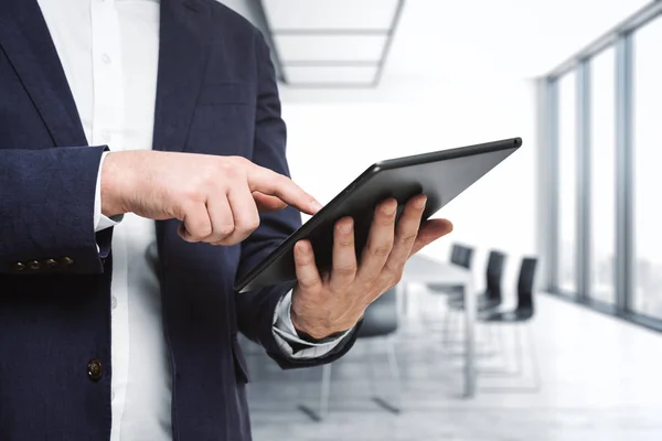 Man presses on the screen of a digital tablet in sunny boardroom, close up. Online technology concept