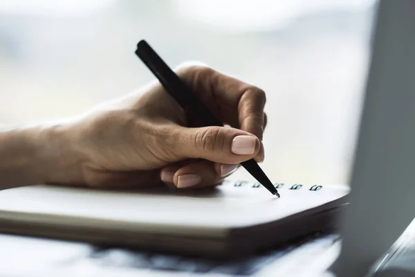 A mulher de negócios escreve com uma caneta no diário no teclado de computador portátil em um escritório ensolarado, conceito de negócios e educação. Fechar — Fotografia de Stock