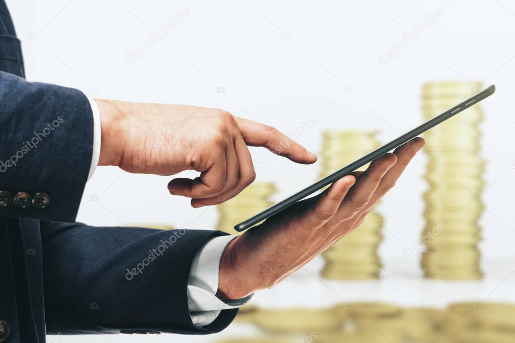 Businessman hand clicks on the screen of a digital tablet on the background of stacks of gold coins, close up. Online trading Concept