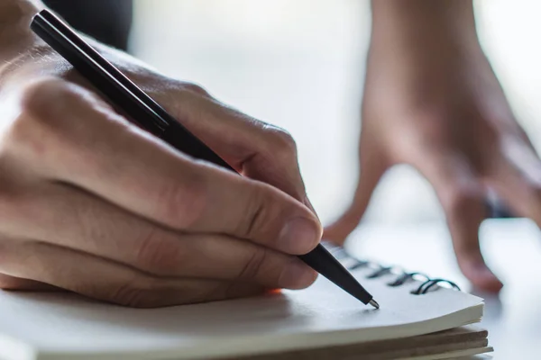 O homem escreve com uma caneta no bloco de notas em um escritório ensolarado, conceito de negócios e educação. Fechar — Fotografia de Stock