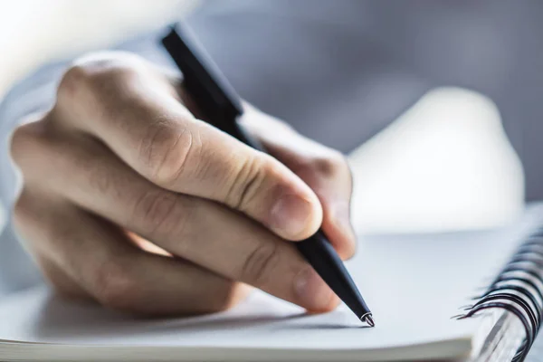 De mens schrijft met een pen in notitieblok in een zonnig kantoor-, bedrijfs- en onderwijsconcept. Sluiten. — Stockfoto