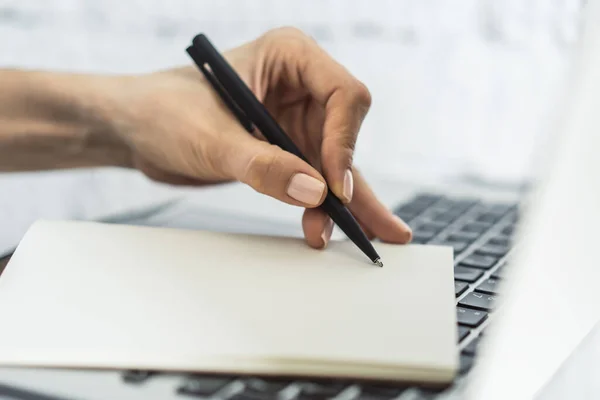 Empresaria escribe con un bolígrafo en el diario en el teclado del ordenador portátil en una oficina soleada, negocio y concepto de educación. De cerca. — Foto de Stock