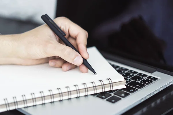 El hombre escribe con un bolígrafo en el diario en el teclado portátil en una oficina soleada, negocio y concepto de educación. De cerca. — Foto de Stock