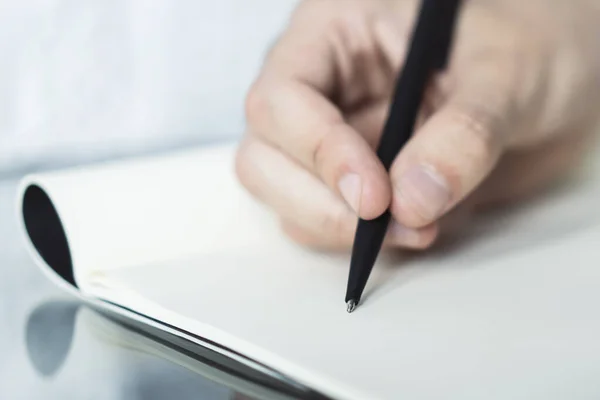 De mens schrijft met een pen in notitieblok in een zonnig kantoor-, bedrijfs- en onderwijsconcept. Sluiten. — Stockfoto