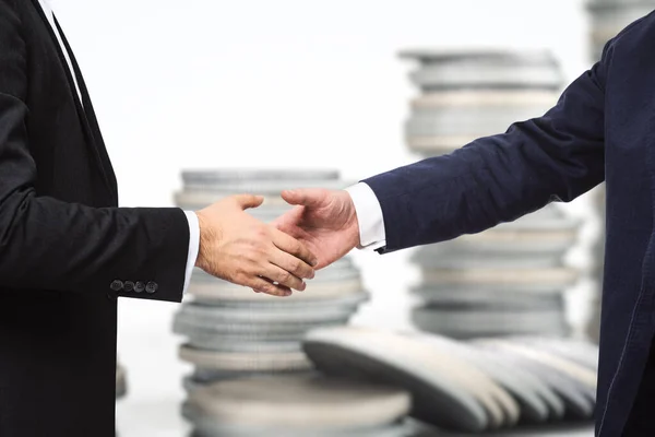 Два бизнесмена пожимают друг другу руки на фоне растущих пачек монет, инвестиционной концепции, крупным планом — стоковое фото