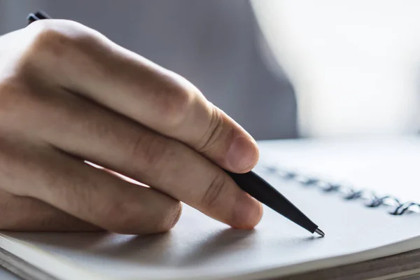 Man schrijft met een pen in notitieboekje in een zonnig kantoor-, bedrijfs- en onderwijsconcept. Sluiten. — Stockfoto