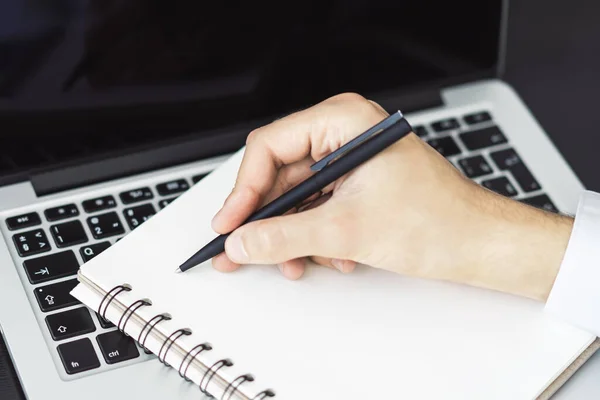 El hombre escribe con un bolígrafo en bloc de notas en el teclado del ordenador portátil en una oficina soleada, negocio y concepto de educación. De cerca. — Foto de Stock