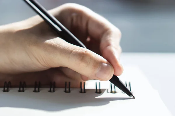 O homem escreve com uma caneta no caderno em um escritório ensolarado, conceito de negócios e educação. Fechar — Fotografia de Stock
