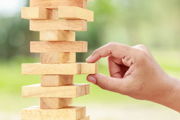 Hand holding blocks wood game (jenga) on blurred green backgroun