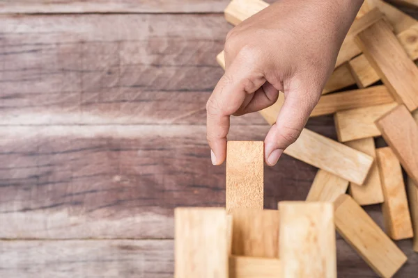 Mano sosteniendo bloques juego de madera (jenga) sobre fondo de madera tablón —  Fotos de Stock