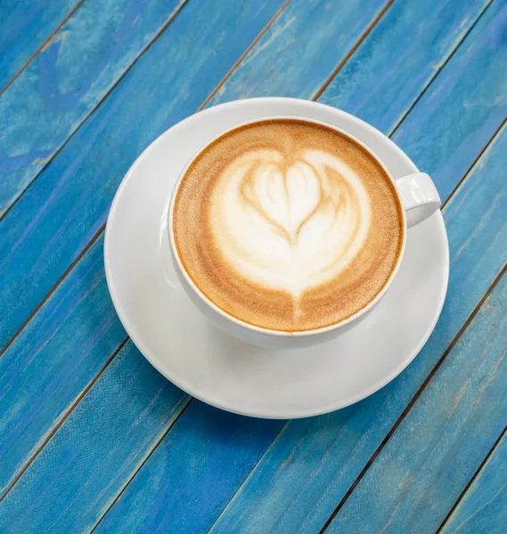 Bovenaanzicht hete latte koffie in witte cup op blauw vintage houten ta — Stockfoto