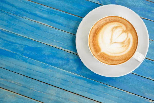 Von oben heißen Latte-Kaffee in weißer Tasse auf blauem Vintage-Holz ta — Stockfoto