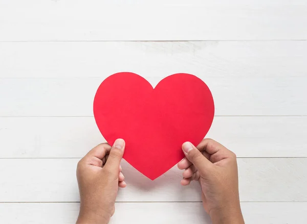 Vista dall'alto mano tenendo carta rossa del simbolo del cuore. Su legno bianco — Foto Stock
