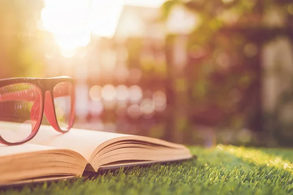 Glasses and book on green grass with blur and bokeh in sunrise t — Stock Photo, Image