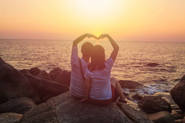 Влюбленная пара, сидящая на скале с видом на океан и закат — стоковое фото