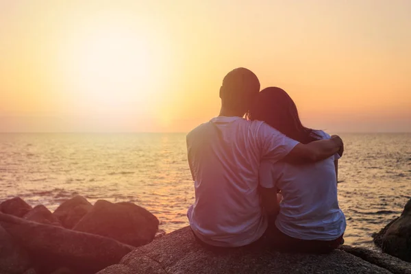 Couple d'amour assis sur le rocher à l'océan et au coucher du soleil vue — Photo