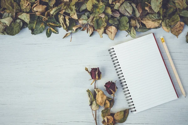 Notizbuch und trockene Rosenblüte auf weißem Holzdeck mit leerem Wellnessbereich — Stockfoto
