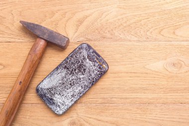 Kırık siyah smartphone ve ahşap masa arka plan üzerinde çekiç