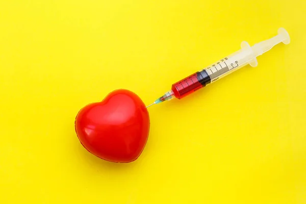 Jeringa dar medicamento a la forma del corazón rojo sobre fondo amarillo. U —  Fotos de Stock