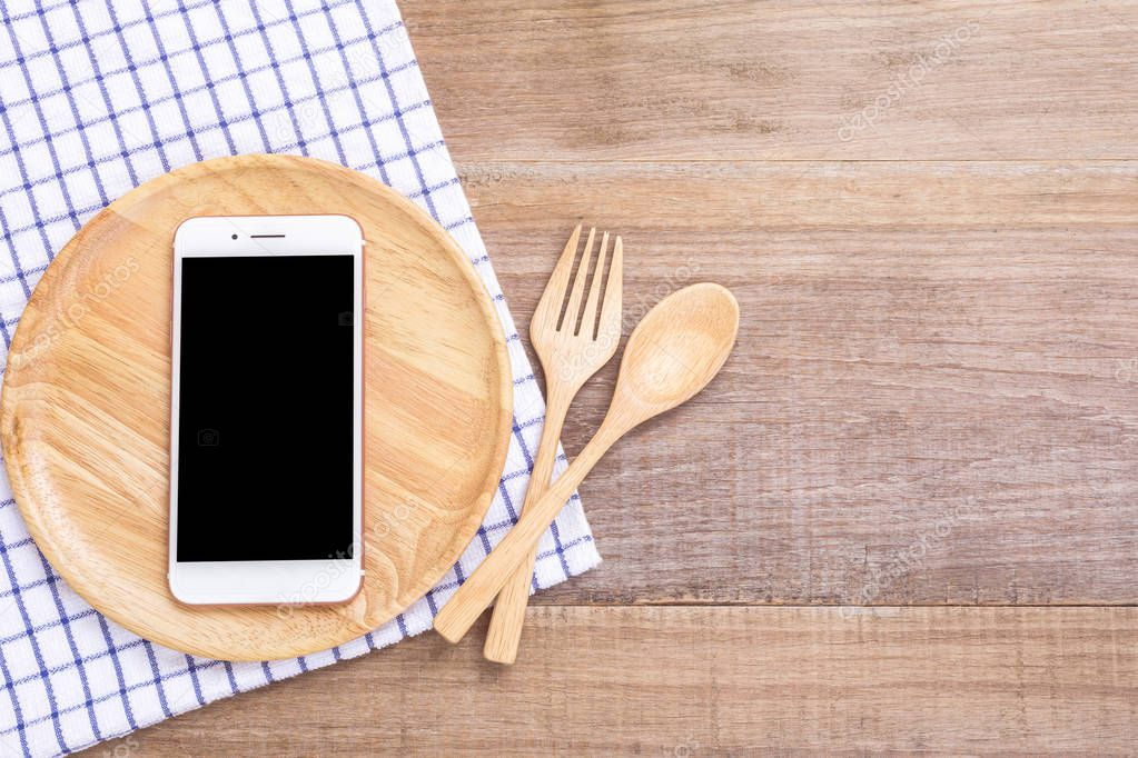 Smartphone in wooden dish, spoon and fork on wooden plank backgr
