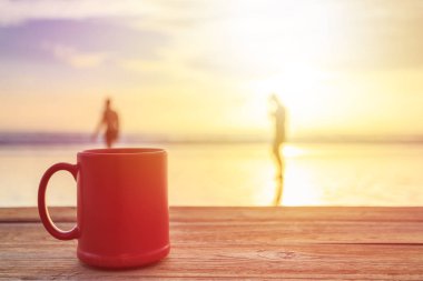 Kırmızı kahve fincanı gündoğumu veya günbatımı Plajı'nda ahşap masa üzerinde