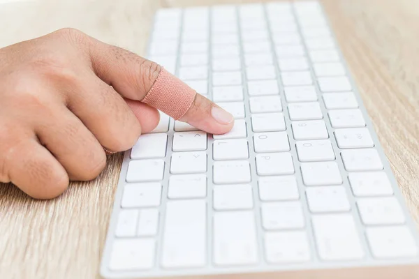 Hand with injury on finger using white computer keyboard on wood