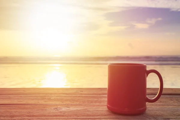 Xícara de café vermelho na mesa de madeira ao pôr do sol ou ao nascer do sol praia — Fotografia de Stock