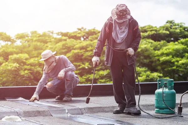 Grupo de trabajadores instalando lámina de alquitrán en la azotea del edificio . — Foto de Stock