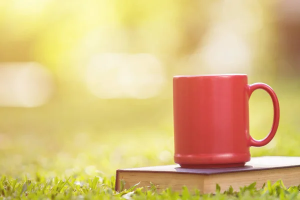 Taza de café de cerámica roja y viejo libro en jardín verde por la mañana t —  Fotos de Stock