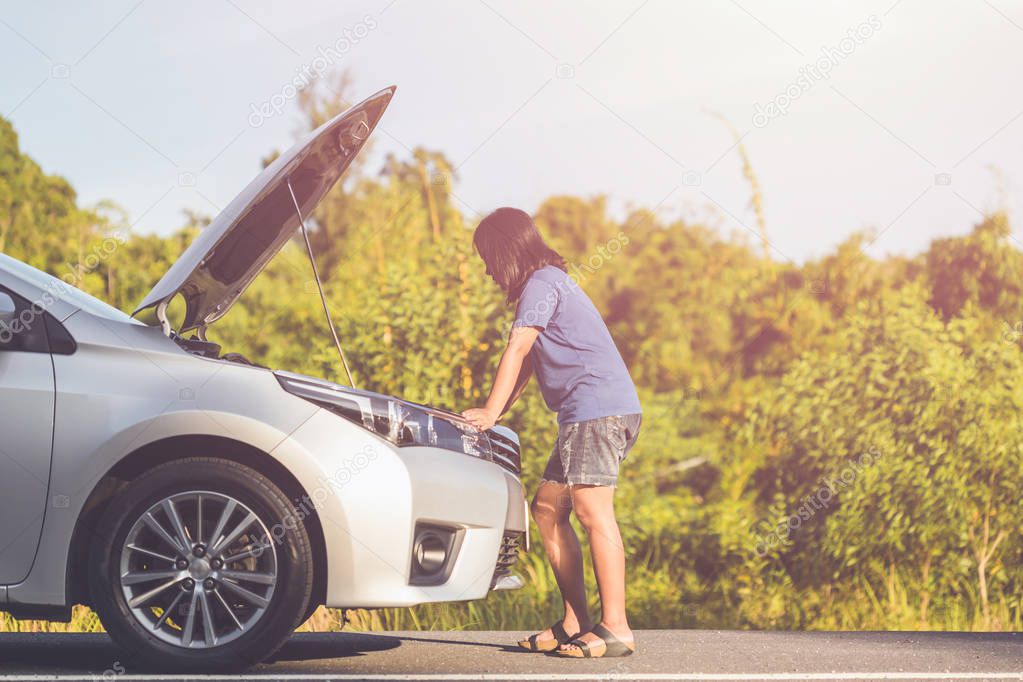 Woman using smartphone in front of her broken car on the road. C