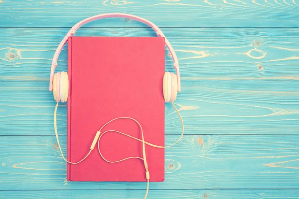 Книга и новый современный розовый музыкальный наушник на голубой деревянной доске — стоковое фото
