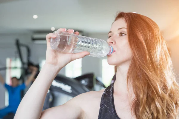 Spor salonunda egzersiz yaparken genç Kafkas kadın içme suyu