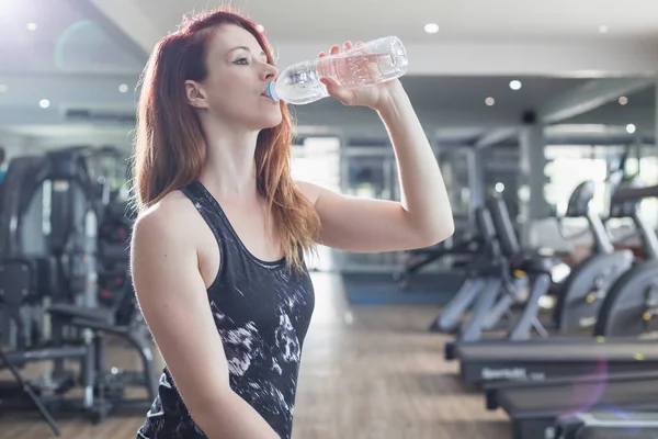 Spor salonunda egzersiz yaparken genç Kafkas kadın içme suyu