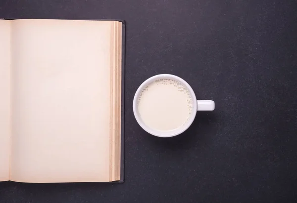Γάλα λευκό γυαλί και ανοιχτό βιβλίο στο μαύρο πέτρινο τραπέζι. Το Top view — Φωτογραφία Αρχείου