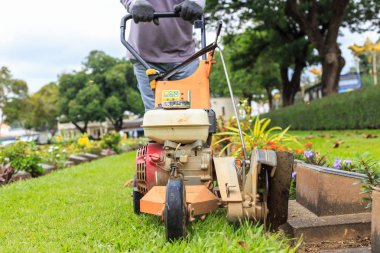 A man mowing grass in the public garden. Outdoor working  clipart