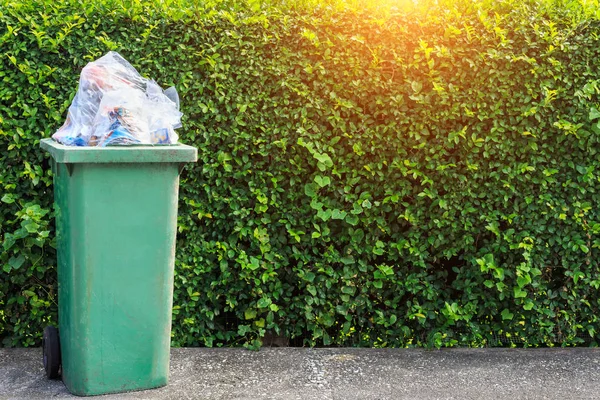 Полный мусор в зеленом мусорном баке на дороге рядом с зеленым — стоковое фото