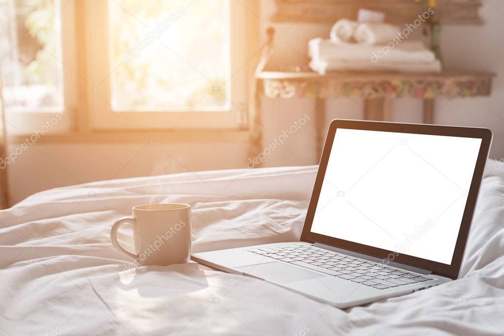 White coffee cup and laptop on the bed in morning time with soft