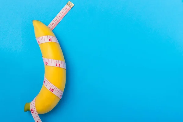 Yellow banana with measurement tape on blue background. Men peni — Stock Photo, Image