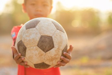 Genç Asyalı çocuk yaşlı ve kirli klasik futbol topuyla oynuyor.