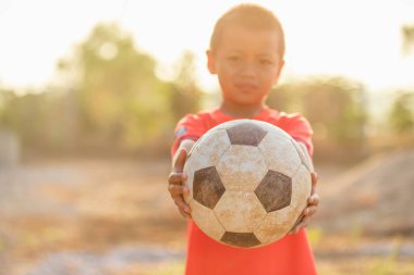 Genç Asyalı çocuk yaşlı ve kirli klasik futbol topuyla oynuyor.