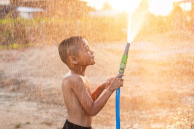 Mutlu Asyalı küçük çocuk yıkamak için hortum ve spreyle su oynuyor.