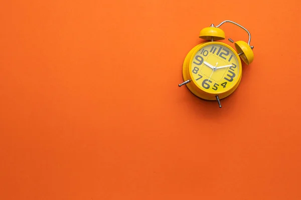 Relógio de alarme amarelo no meio do fundo laranja — Fotografia de Stock