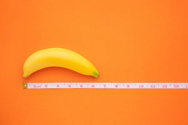 Žlutý banán s měřicí páskou na oranžovém pozadí. Men pe — Stock fotografie