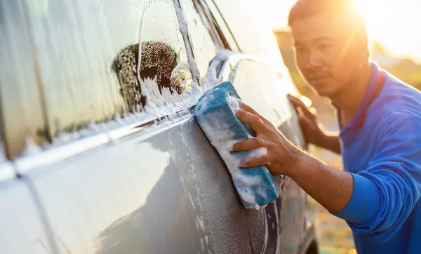 Asyalı adam arabayı yıkamak için sabunla mavi sünger kullanıyor. — Stok fotoğraf